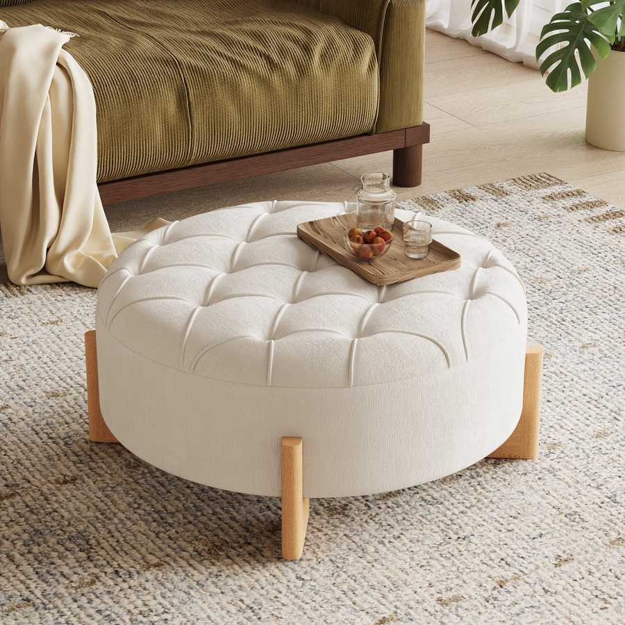 Round white ottoman with wooden legs in a living room setting.