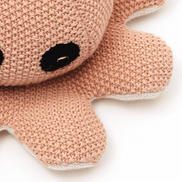 Close-up of peach knitted octopus plush toy with black embroidered eyes, soft baby toy