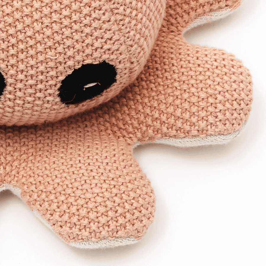 Close-up of peach knitted octopus plush toy with black embroidered eyes, soft baby toy