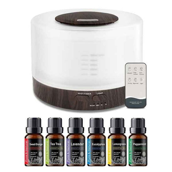 A white and dark wood essential oil diffuser with a matching remote control, shown above six essential oil bottles labeled Sweet Orange, Tea Tree, Lavender, Eucalyptus, Lemongrass, and Peppermint on a white background.