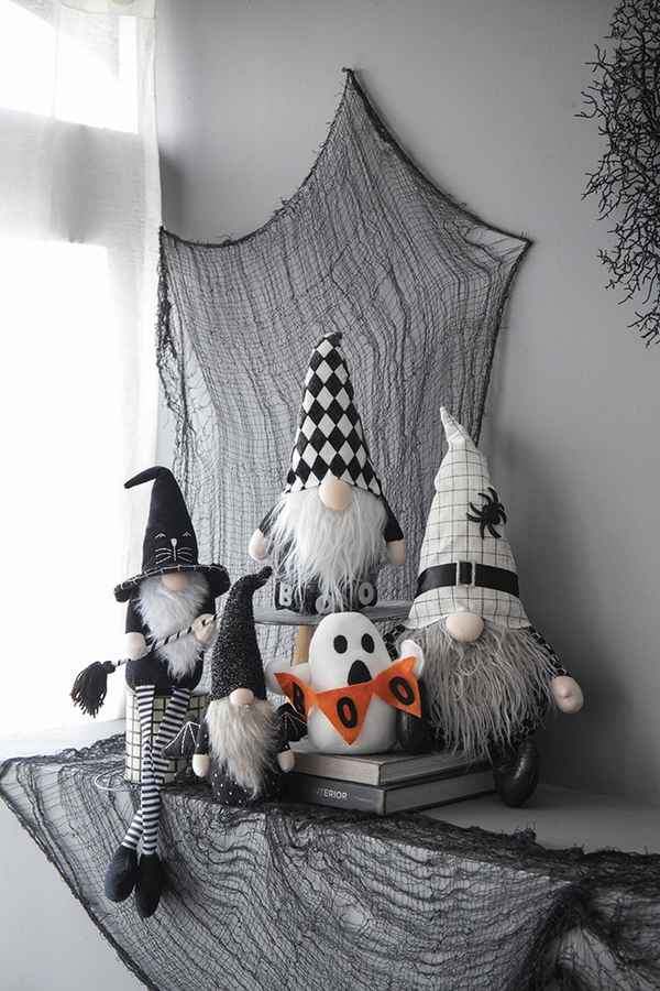 Halloween-themed home decor featuring black and white gnome figures with pointy hats, a ghost, and black web accents on a dark table.