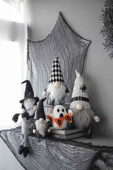 Halloween-themed home decor featuring black and white gnome figures with pointy hats, a ghost, and black web accents on a dark table.