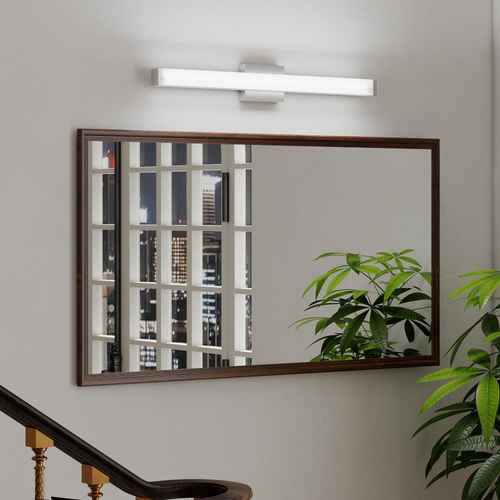 Rectangular mirror with wooden frame on a wall with a light fixture above, featuring a cityscape reflection.