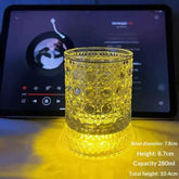 A clear cut-glass tumbler with a warm yellow LED light glowing through it, placed in front of a tablet player. White text in the lower right lists dimensions: bowl diameter 7.
