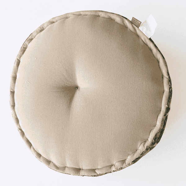 Round beige cushion with a visible brand tag on a white background