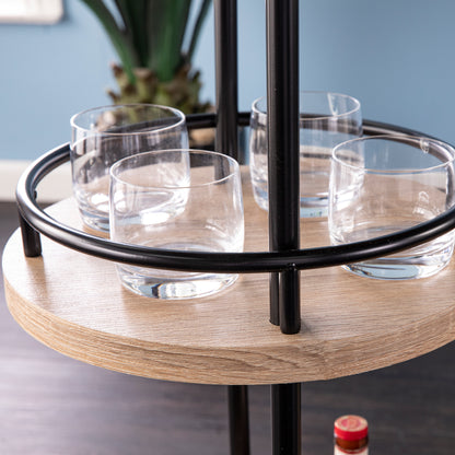 Detail of round side shelf on Dagney Wine Bar Table Storage with black metal rail holding four glass tumblers securely in modern style.