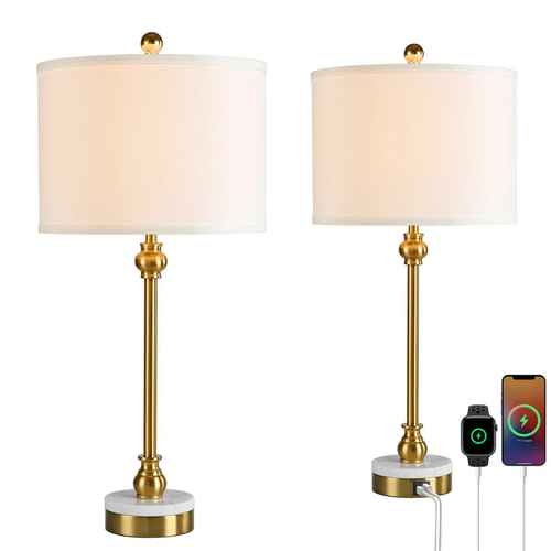 Two matching table lamps with white drum shades, gold-toned stems and finials, and round white marble-look bases, shown on a white background. One lamp is fully visible, and the other is shown with a power strip and charging cables connected, alongside a smartwatch and smartphone screen.