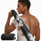 Man with soap suds on his back holding a black mesh scrubber.