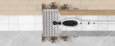 A wet-dry floor cleaner shown from above, with a white and black head lifting dark dirt over a tiled floor transition between wood and marble surfaces.