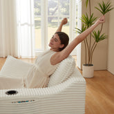 Woman relaxing on a white inflatable massage chair in a bright room with large windows.