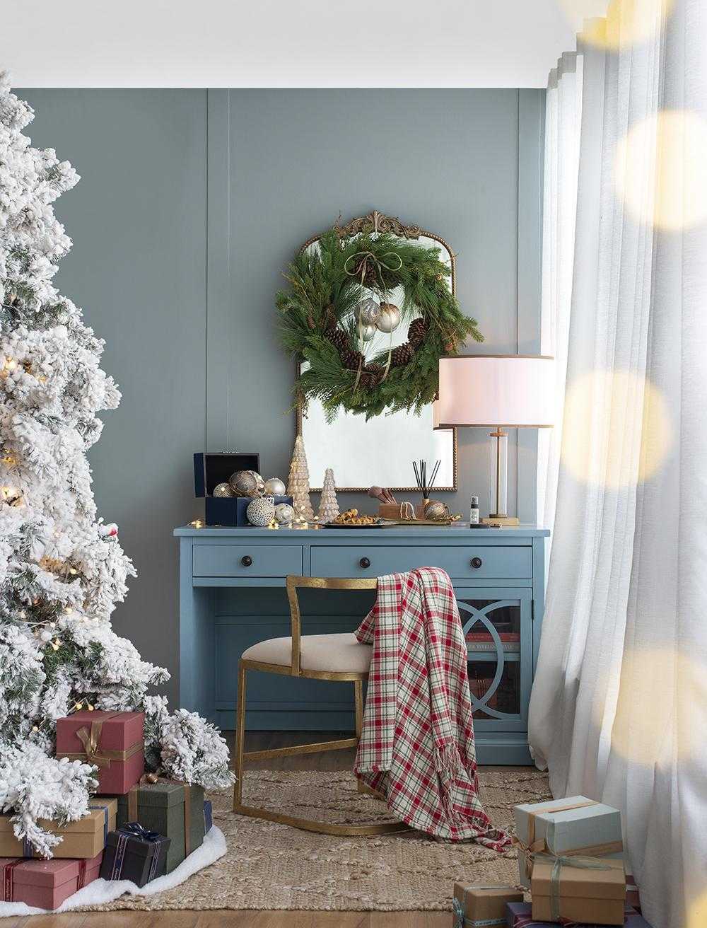 Decorated living room with Christmas tree, wreath, and gifts against a blue wall.