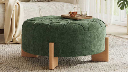 Green tufted ottoman with wooden legs in a living room setting.