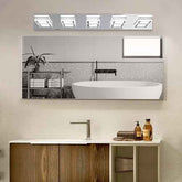 A rectangular wall-mounted bathroom mirror with a built-in light fixture above it, shown installed above a vanity in a real bathroom setting. The mirror reflects a bathtub, tiled wall, and shelf, while the room itself has beige walls and a wood-and-white cabinet below.