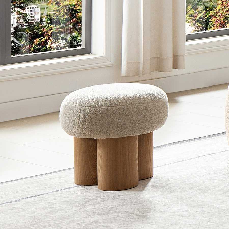 Round ottoman with wooden legs in a room with a window and curtains.