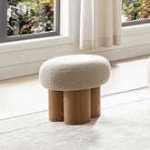 Round ottoman with wooden legs in a room with a window and curtains.