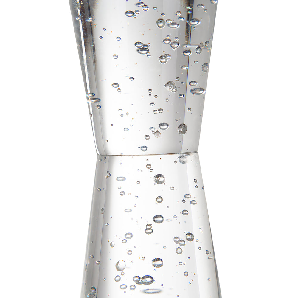 A clear glass jigger with a double-cone shape, filled with small bubbles and photographed against a plain white background.