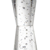 A clear glass jigger with a double-cone shape, filled with small bubbles and photographed against a plain white background.