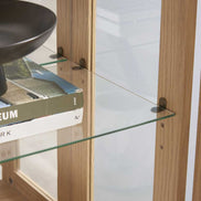 Detail of adjustable glass shelf inside lighted curio cabinet, supported by metal pegs for flexible display options.