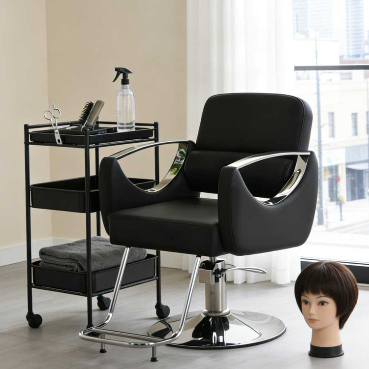 Black salon chair with a cart and mannequin head in a room with large windows.
