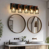 A five-light wall sconce fixture with black metal wire mesh cylindrical shades and warm glowing bulbs, mounted above two round wood-framed mirrors in a bathroom setting.