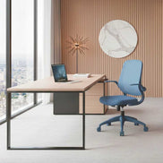 Modern office desk with a blue chair in a room with large windows and decorative wall art.
