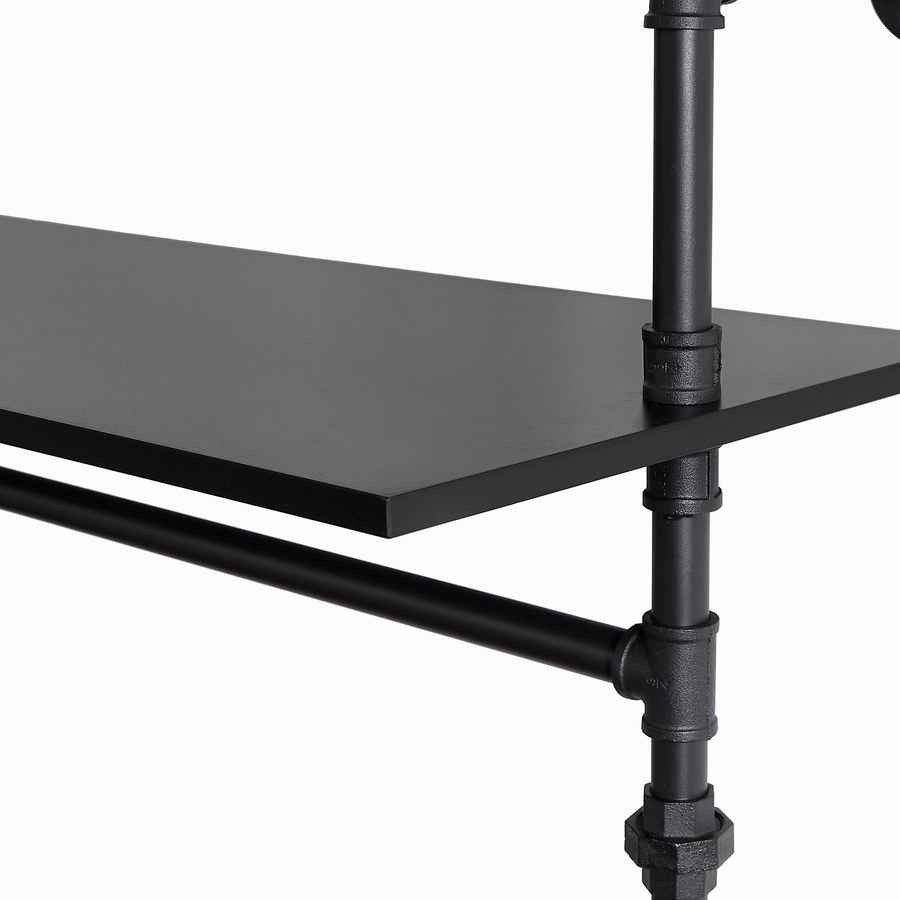 Close-up of black metal pipe fittings on industrial clothes rack with adjustable height, supporting shelves and LED lighting