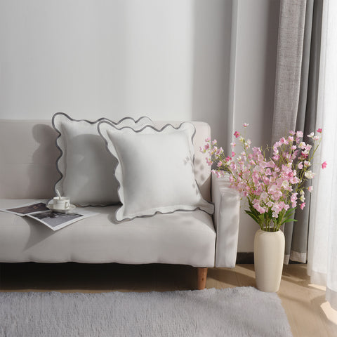 Living room with a gray sofa, decorative pillow, and a vase of pink flowers.