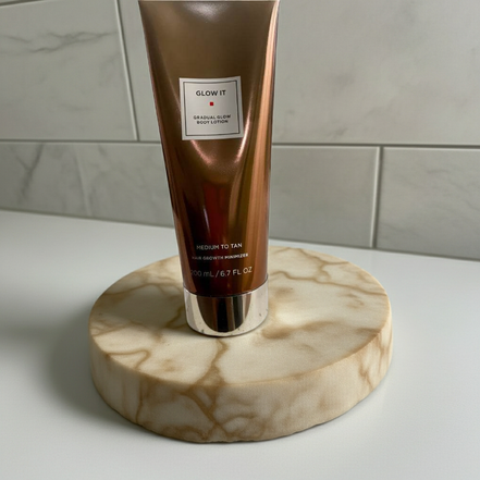 Glow It Gradual Glow Body Lotion Medium to Tan 6.7 fl oz displayed on marble tray, perfect for enhancing natural tan and skin hydration.
