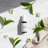 Tea Tree Caffeine Serum lifestyle flat lay on marble with green tea leaves and white flowers