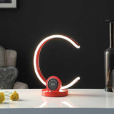 Modern LED desk lamp with a red base on a white surface, dark background