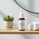 Skincare serum bottle on a wooden surface with a plant and towel in the background