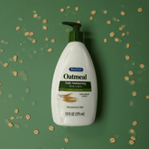 Oatmeal body lotion bottle with pump on a green background with scattered oats.